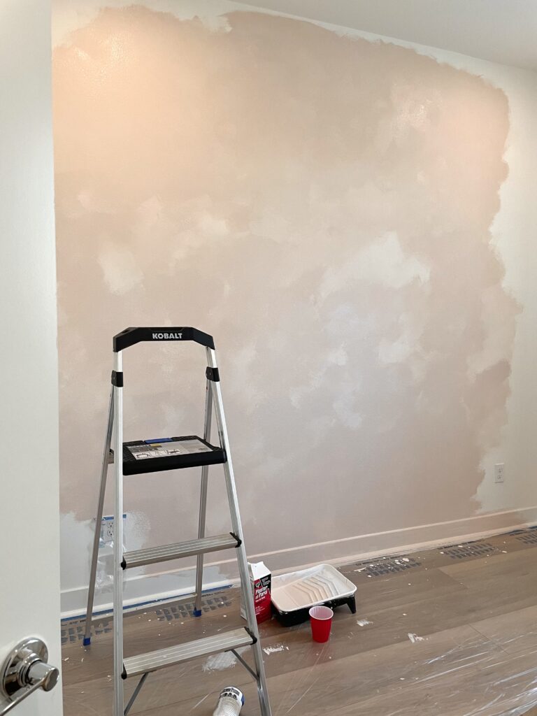 Painting a pink limewash wall with loose cross-hatch brush strokes using a wide brush