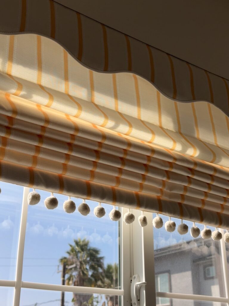 yellow striped scalloped Roman shade installed in a kitchen window frame